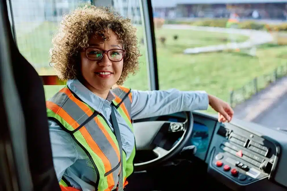 Conductrice de bus souriante au volant en gilet de sécurité, illustrant la capacité de transport de personnes